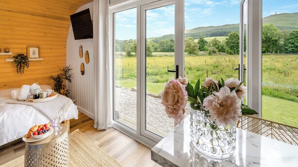 A room with a bed, breakfast tray, flowers, and a large window with a countryside view. - Freedom Fields - Bluebell (Straiton, near Maybole)
