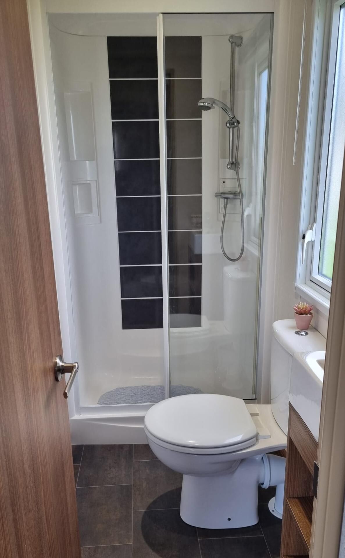 A modern bathroom with a glass-enclosed shower, a white toilet, and a sink with a window above it.