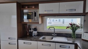 A modern kitchen with a built-in microwave, a coffee maker, and a window with a view of a house. - Stunning Seaside Lodge Nr New Forest 2 bed (New Milton)