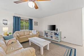 A living room with a sofa, a coffee table, a television on a stand, and a ceiling fan.
