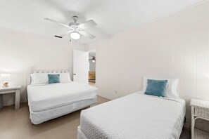 Un dormitorio con dos camas, un ventilador de techo y una mesita de noche con lámpara.