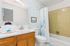 Un baño con un lavabo blanco, tocador de madera, inodoro y zona de ducha con pared de azulejos color beige.