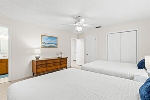 Une chambre avec deux lits, un ventilateur de plafond, une commode et un tableau au mur.