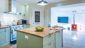 Een moderne keuken met een centraal eiland, inbouwapparatuur en een rode houtkachel.