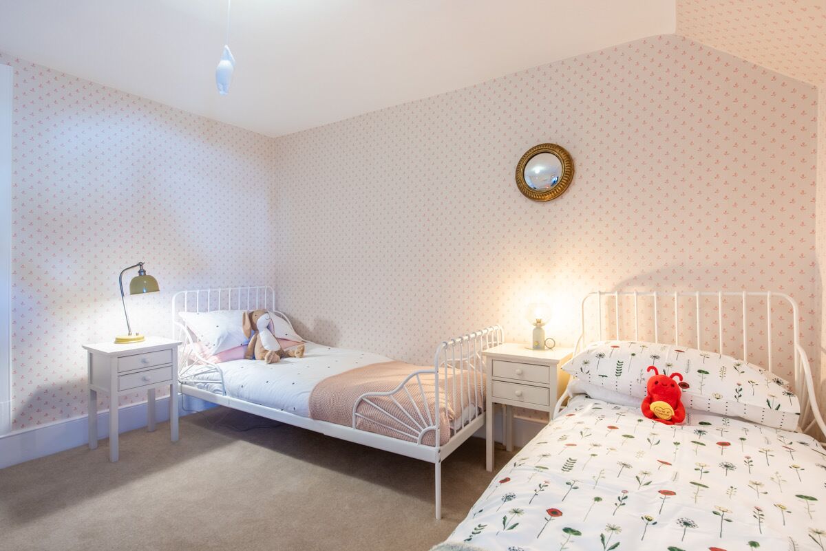 A bedroom with two beds, a bedside table with a lamp, a mirror, and a teddy bear on one bed.