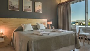 Una cama bien hecha con almohadas y toallas dobladas, una mesita de noche con una lámpara, y cuadros en la pared.