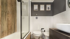Un baño moderno con bañera, dos inodoros, ducha y tocador con lavamanos.