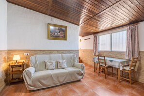 A living room with a sofa, a table, chairs, a lamp, a painting, and a window with curtains. - Holiday Home 'Casa Pepita' with Mountain View, Private Pool and Wi-Fi (Cacín)