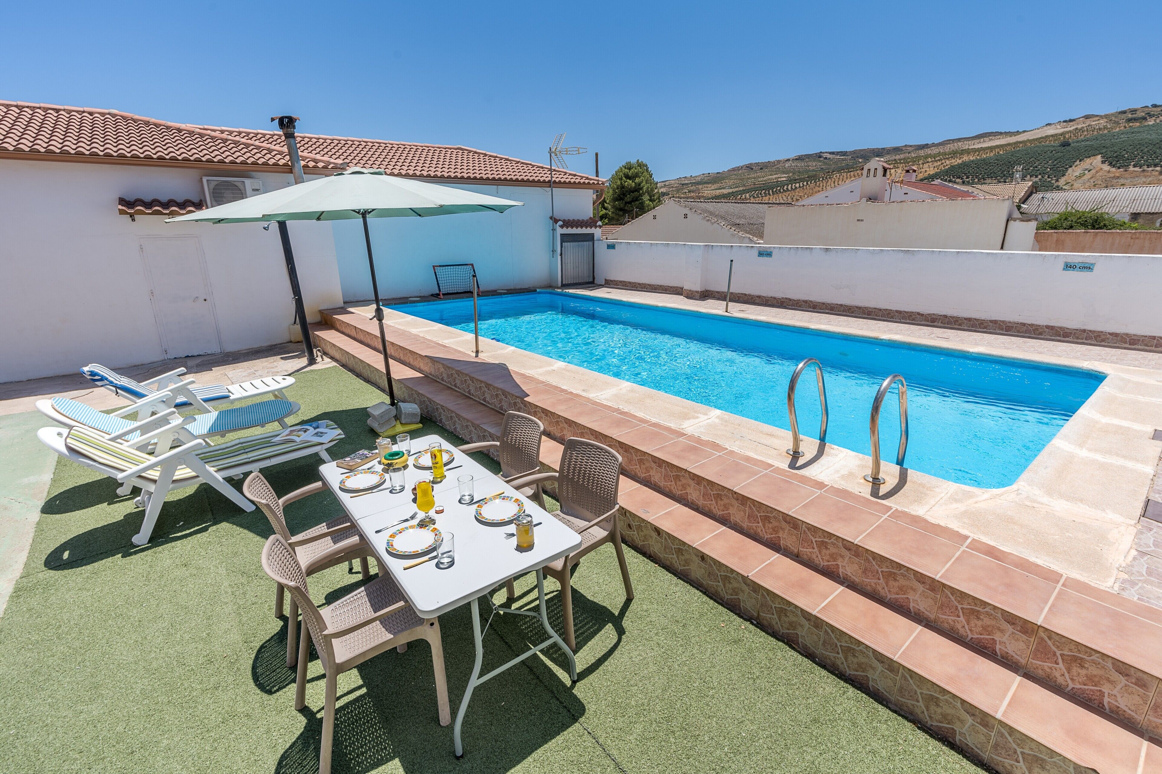 A rooftop swimming pool with a table and chairs, a covered umbrella, and a view of the surrounding landscape.