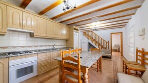 A kitchen with wooden cabinets, a granite countertop, a stove, and a dining area with a table and chairs. - Holiday Home 'Casa Rural Las Cales' with Mountain View, Private Pool and Wi-Fi (VELEZ-RUBIO)