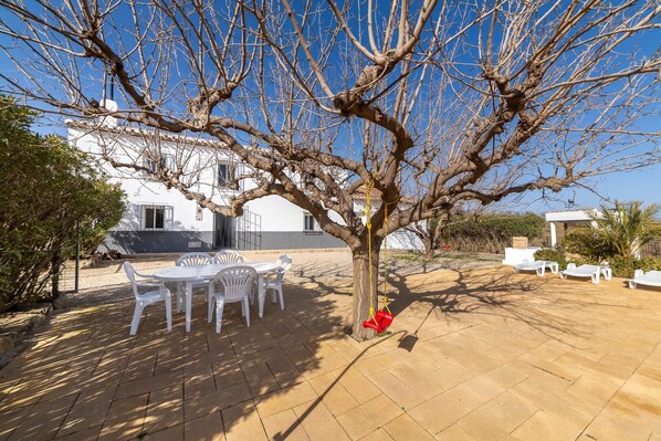 A patio with white plastic chairs and a table, a tree with a swing, and a white building in the background. - Holiday Home 'Casa Rural Las Cales' with Mountain View, Private Pool and Wi-Fi (VELEZ-RUBIO)