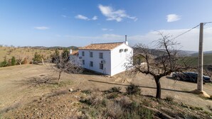 A white building with a tiled roof, surrounded by a hilly landscape, a tree, and a parked car. - Holiday Home 'Casa Rural Las Cales' with Mountain View, Private Pool and Wi-Fi (VELEZ-RUBIO)