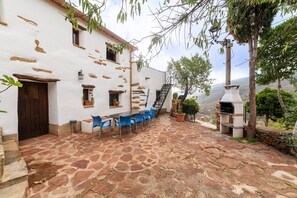 A stone-paved courtyard with a white building, blue chairs, and a stone oven. - Holiday Home 'Casa Rural Albaida' with Mountain View, Shared Pool and Wi-Fi (LAROYA)