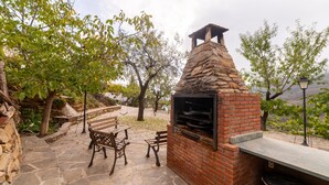 Eine Terrasse im Freien mit Steinboden, einem Backstein-Barbecue und Holzmöbeln.