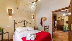 Ein Schlafzimmer mit einem Bett, einer roten Decke, einem weißen Kissen, einem Nachttisch mit einer Pflanze und einem an der Wand hängenden Hut.