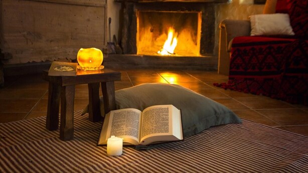 Ein gemütliches Zimmer mit Kamin, einem Buch, einer Kerze und einem gemusterten Teppich.