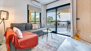A modern living room with a sofa, a small round table, a floor lamp, and a large sliding glass door leading to an outdoor area.