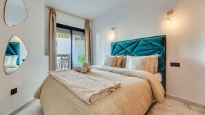 A bedroom with a bed, a window with curtains, a wall-mounted mirror, and a bedside table.