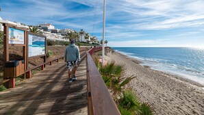 A wooden boardwalk leading to a beach with a clear sky and a signboard.