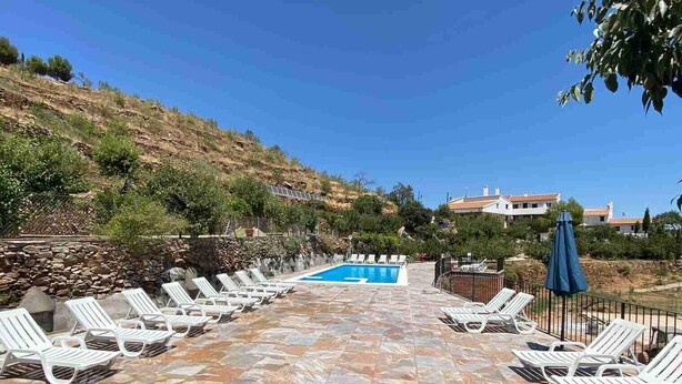 Un espace piscine doté d’un sol en pierre, de chaises longues blanches et surplombé d’un ciel d’un bleu limpide.