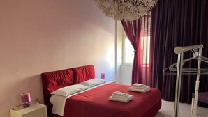 Un lit bien fait, avec une literie rouge, une table de chevet avec une lampe et une fenêtre avec des rideaux.