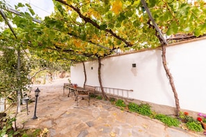 A stone-paved patio with a bench and table, surrounded by greenery and a white wall. - Holiday Home 'Casa Rural San Marcos' with Mountain View, Shared Pool and Wi-Fi (Laroya)