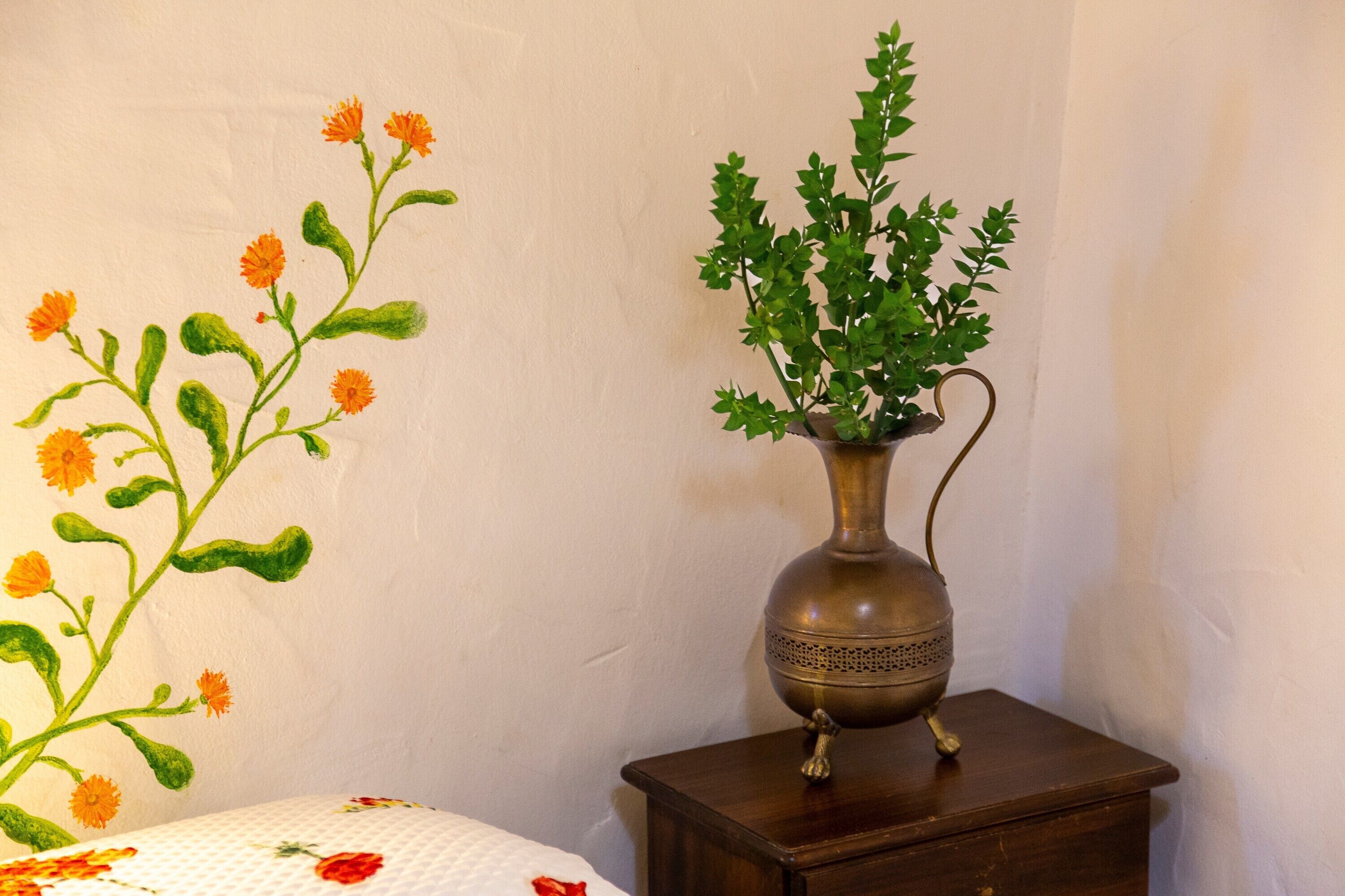 A vase with green foliage and a branch with orange flowers on a wooden nightstand.
