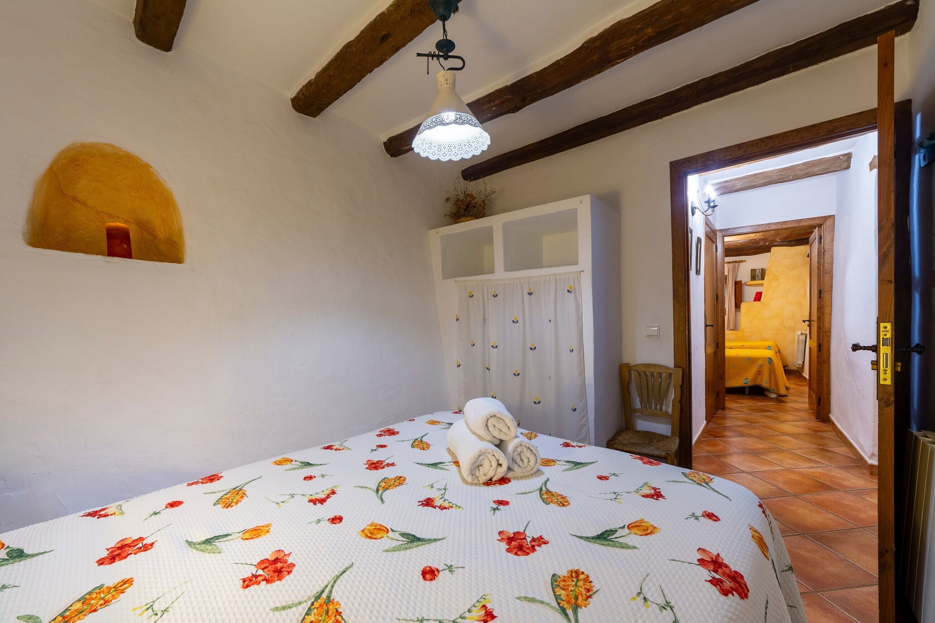 Un dormitorio con colcha estampada floral, techo de madera, un armario y una puerta que da a otra habitación.