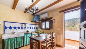 A kitchen with a tiled backsplash, wooden chairs, a dining table, and a view through a window. - Holiday Home 'Casa Rural Padre Ramon' with Mountain View, Shared Pool and Wi-Fi (Laroya)