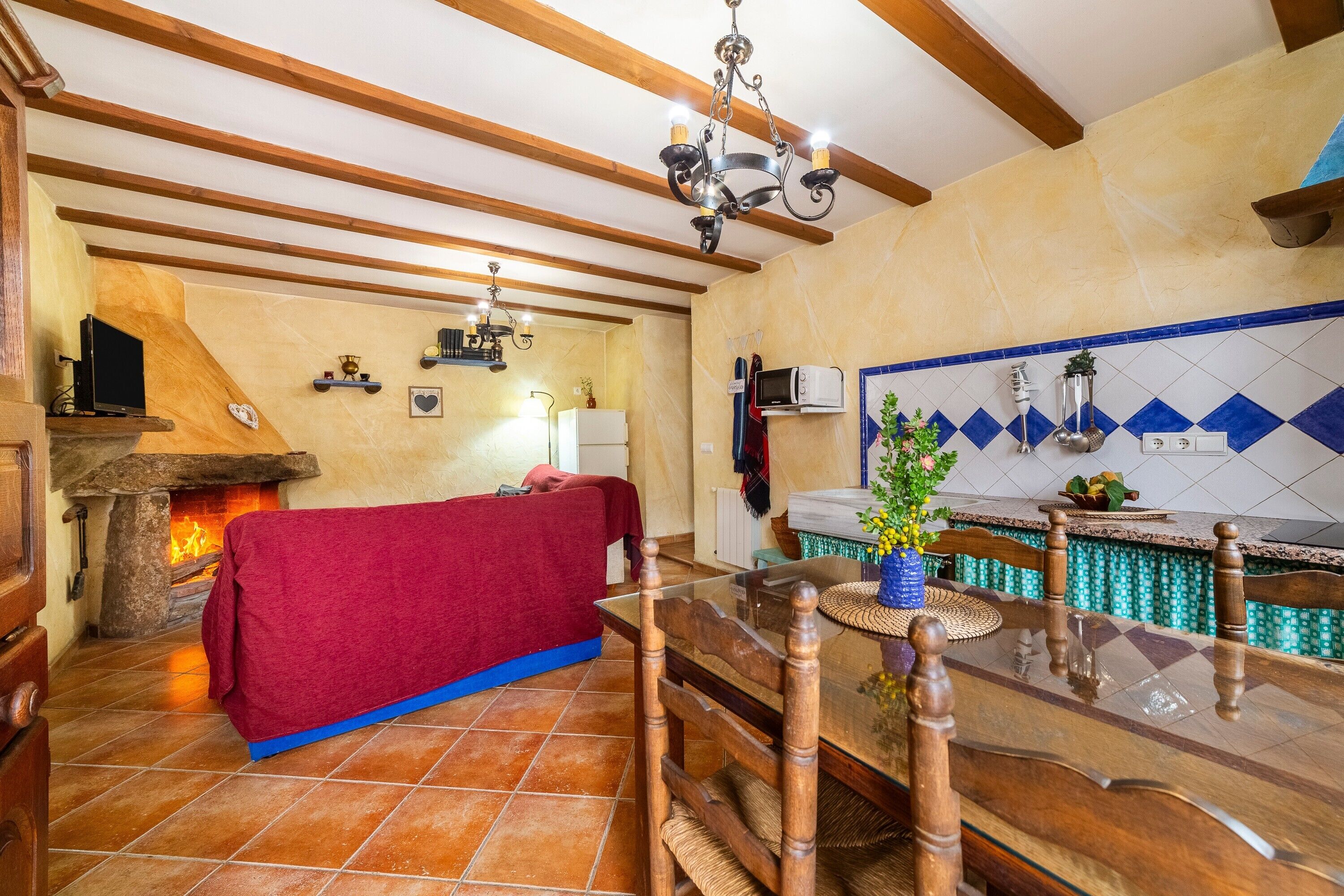 Una cocina acogedora con chimenea, vigas de madera, una mesa de comedor y salpicadero de azulejos.