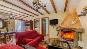 A living room with a fireplace, a red sofa, a dining area with a wooden table, and a kitchen visible through an open door. - Holiday Home 'Casa Rural Padre Ramon' with Mountain View, Shared Pool and Wi-Fi (Laroya)