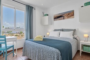 Un dormitorio con cama, escritorio, silla, ventana con vistas y mesita de noche con lámpara.