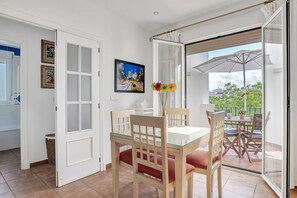 Un comedor con mesa y sillas de vidrio, un jarrón con flores y vistas al exterior.