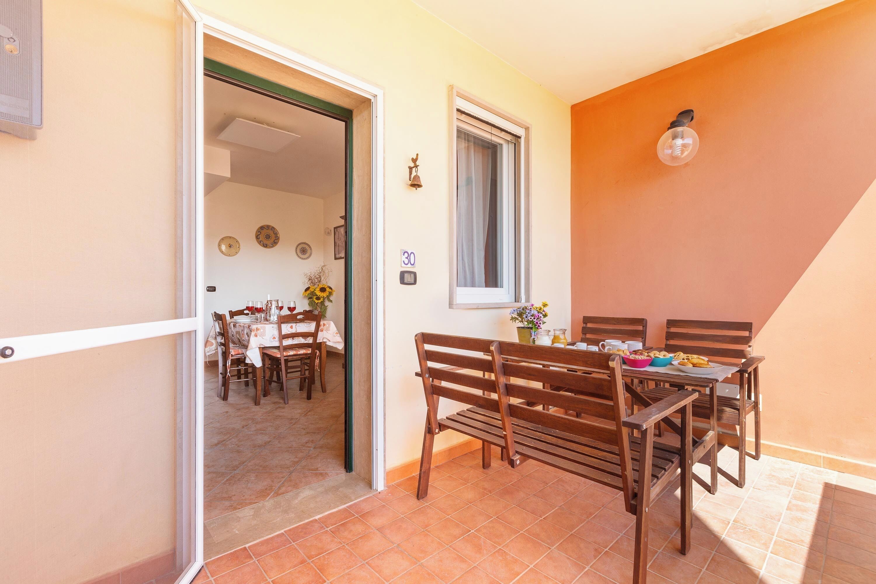 A dining area with a table set for four, wooden chairs, a bench, and a window with a curtain.