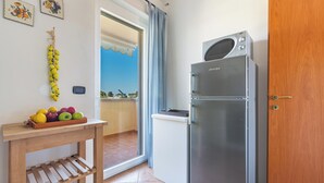 A compact kitchen with a refrigerator, a wooden table with fruits, and a view through a glass door.