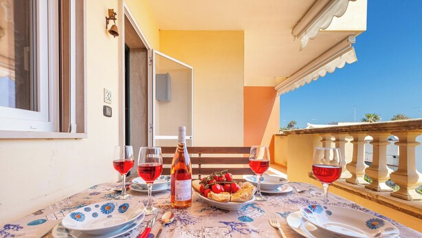 A balcony with a table set for a meal, featuring plates, glasses, and a bottle of wine.
