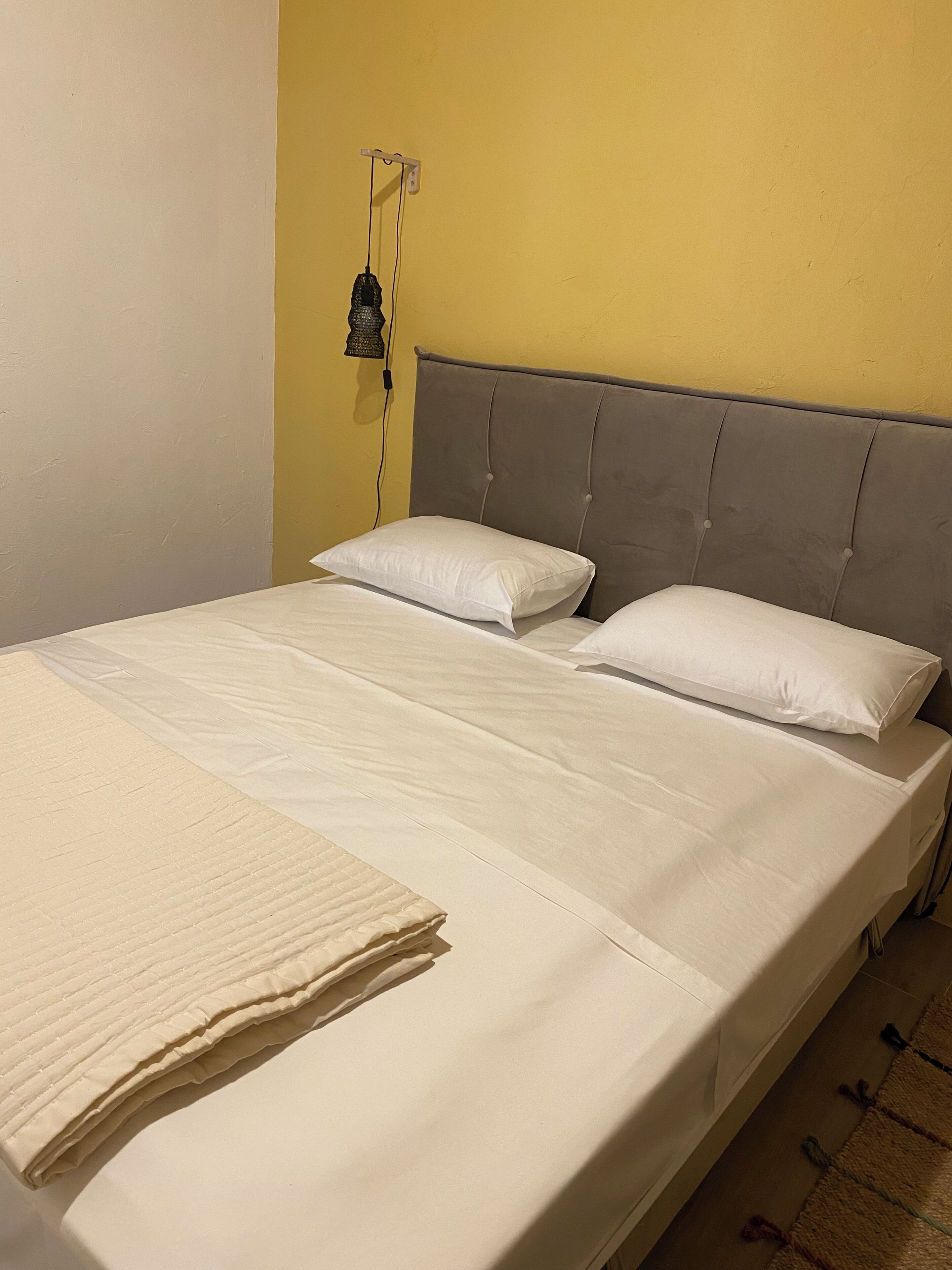 Una cama con cabecera gris, ropa de cama blanca y una colcha.