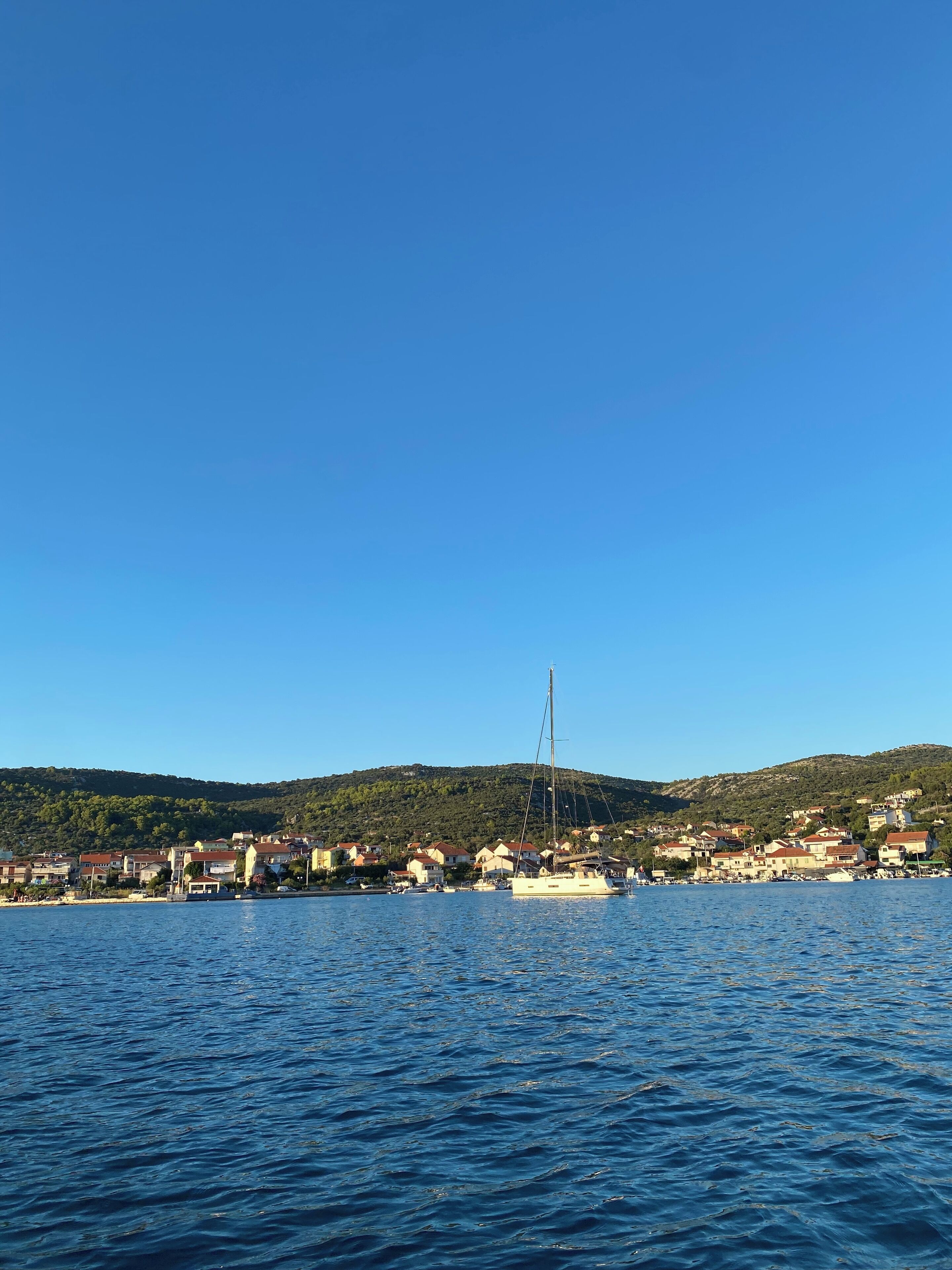 A coastal town with a marina, houses, and hills in the background.