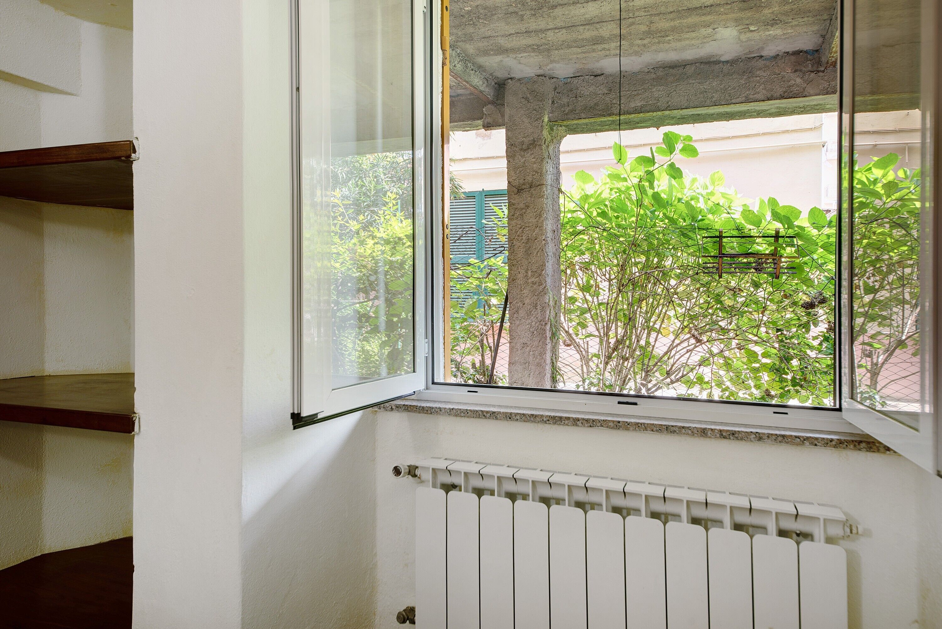 A room with a window overlooking a balcony, a radiator, and a wooden shelf.