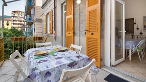 An outdoor dining area with a table set for two, a balcony with yellow shutters, and a view of a cityscape. - Apartment 'Levanto A 50 Metri' with Private Terrace and Wi-Fi (Levanto)