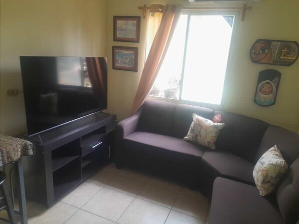 A living room with a flat-screen TV, a sofa, and a window with curtains.