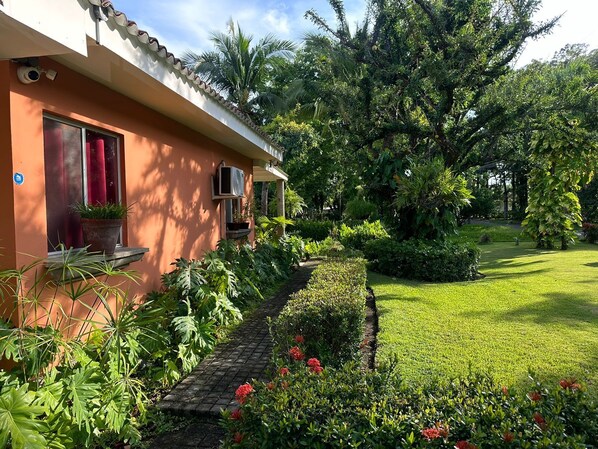 A house with a paved pathway leading to a door, surrounded by lush greenery and a well-maintained lawn.