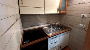 Eine kleine Küche mit eingebautem Herd, einer Spüle und einem Holzschrank über der Arbeitsfläche.