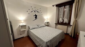 Ein Schlafzimmer mit einem Bett, zwei Nachttischlampen, einem Fenster mit Vorhängen und einer Wandsticker mit einem Skifahrer.