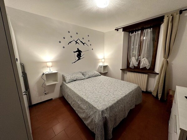 Un dormitorio con cama, dos lámparas de noche, una ventana con cortinas y un adhesivo en la pared de un esquiador.