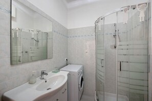 Une salle de bain équipée d’un lavabo, d’un miroir, d’un lave-linge et d’une douche à parois de verre.