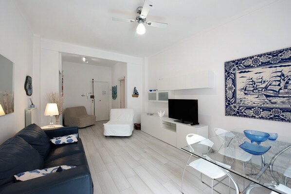 Un salon moderne avec un canapé, une table à manger en verre, un téléviseur et un ventilateur de plafond.