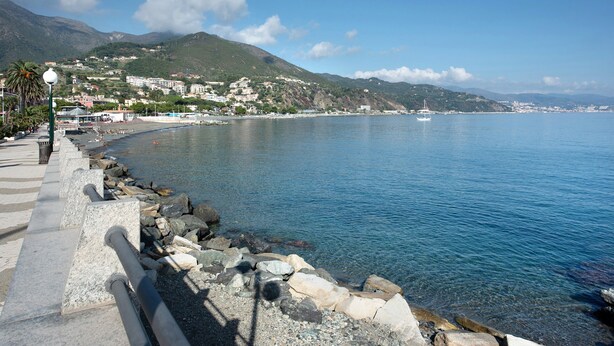 Une promenade en bord de mer, avec une côte rocheuse, une eau d’un bleu limpide et, en arrière-plan, des bâtiments situés sur une colline.