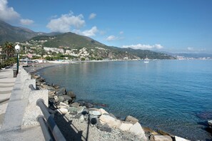 Une promenade en bord de mer, avec une côte rocheuse, une eau d’un bleu limpide et, en arrière-plan, des bâtiments situés sur une colline.