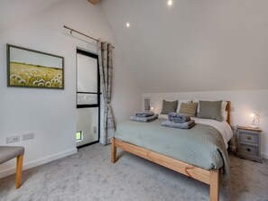 Ein Schlafzimmer mit einem Bett, Nachttischen, einer Bank, einem Gemälde und einem Fenster mit Vorhängen.